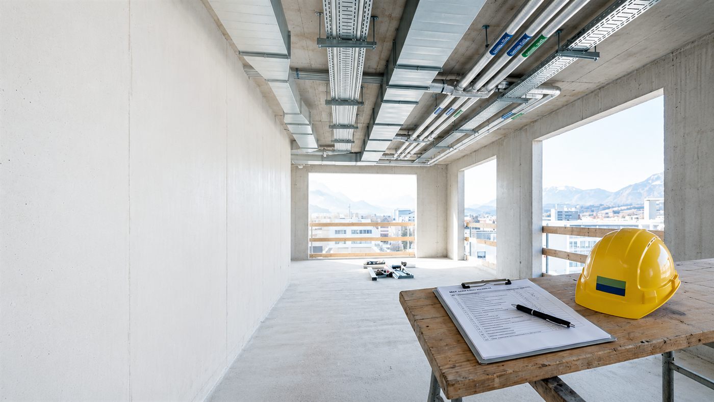 Rohbau mit Haustechnik-Installation an der Decke, Bauhelm und Klemmbrett